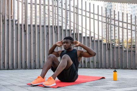 Confident young African man in sportswear doing sit-ups while exercising outdoorsの写真素材