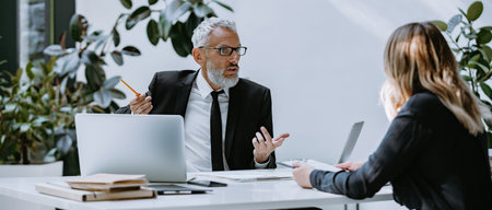 Confident mature man in formalwear interviewing job candidate while sitting at the office desk...