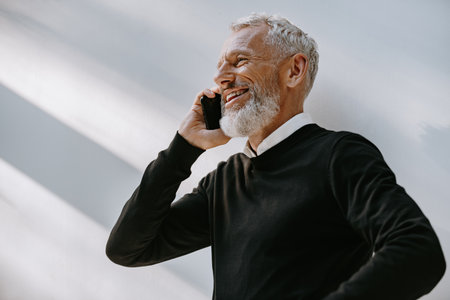 Portrait of happy senior man talking on mobile phone and smiling while standing against the wallの写真素材