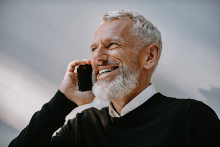 Portrait of happy senior man talking on mobile phone and smiling while standing against the wallの写真素材