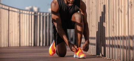 Close-up of African athlete in sportswear tying his shoelaces while preparing for morning jog outdoorsの写真素材