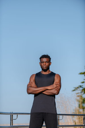 Confident African man in sportswear keeping arms crossed and looking at camera while standing outdoorsの写真素材