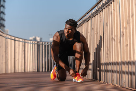 Confident African athlete in sportswear tying his shoelaces while preparing for morning jog outdoors