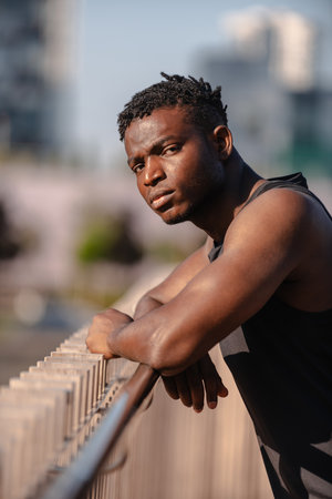 Handsome African man in sportswear leaning at the rail while resting after training outdoorsの写真素材