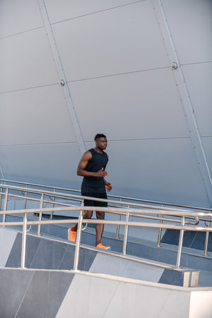 Full length of active African man in sportswear looking concentrated while running outdoors