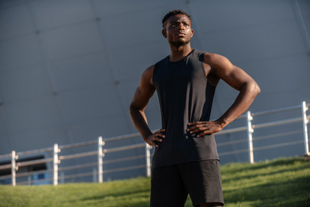 Confident African man in sportswear holding hands on hip while training outdoorsの写真素材