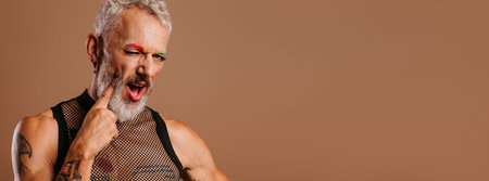 Playful mature gay man with rainbow colored eyebrows touching face with finger against brown...