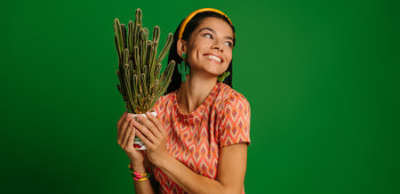 Beautiful young Mexican woman holding cactus and smiling against green backgroundの写真素材