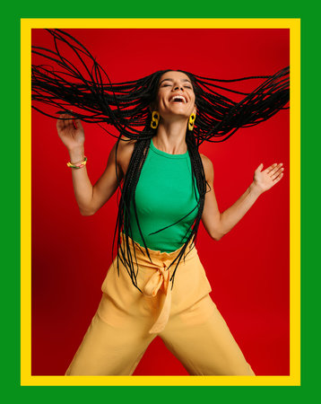 Happy young Hispanic woman with dreadlocs dancing against red background