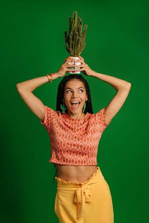 Happy young Mexican woman holding cactus upon head and smiling against green backgroundの写真素材