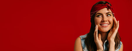 Beautiful young hipster woman with colorful make-up touching face and smiling on red backgroundの写真素材