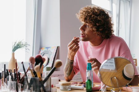 Confident young gay man applying make-up while spending time at homeの写真素材