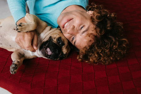 Top view of happy young man petting his cute dog while lying on the floor at home togetherの写真素材
