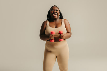 Happy plus size African woman in sportswear exercising with dumbbells on studio backgroundの写真素材