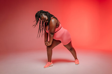 Happy plus size woman in sportswear exercising and looking confident on colorful backgroundの写真素材