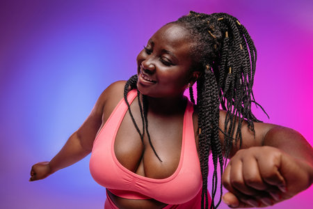Joyful African plus size woman in sportswear dancing and smiling on vibrant backgroundの写真素材