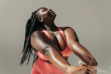 Attractive African plus size woman in sportswear doing stretching exercises in fitness studioの写真素材