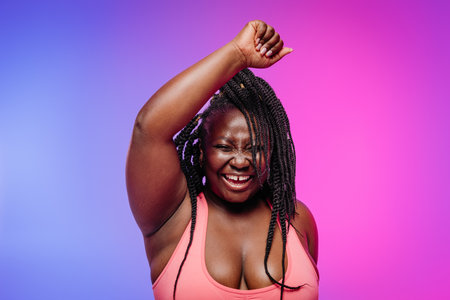 Joyful African plus size woman in sportswear exercising and smiling on vibrant backgroundの写真素材