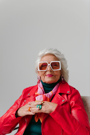 Cool senior woman in fashionable wear sitting in comfortable chair on gray backgroundの写真素材