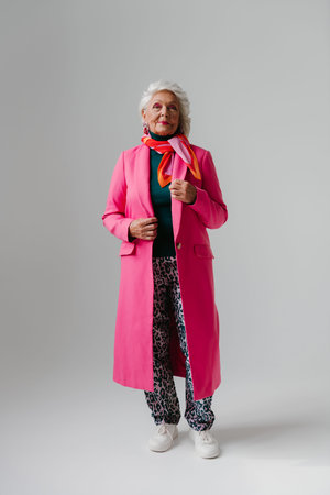 Full length of elegant elderly woman in stylish clothes radiating confidence and self-love on gray backgroundの写真素材