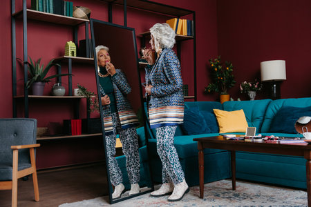 Full length of stylish senior woman doing make-up in front of the mirror at homeの写真素材