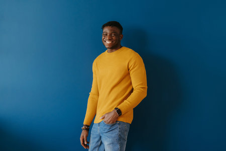Handsome young African man in casual wear smiling while standing on blue backgroundの写真素材