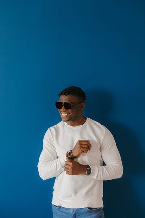 Fashionable young African man in sunglasses smiling while standing on blue background
