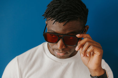 Portrait of fashionable young African man adjusting sunglasses while standing on blue backgroundの写真素材