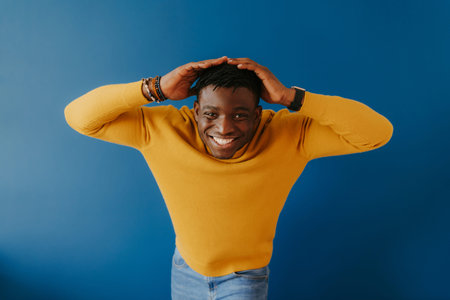 Relaxed young African man in casual wear holding head in hands and smiling while standing