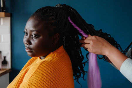Close-up of hairdresser braiding hair to young African woman in salonの写真素材