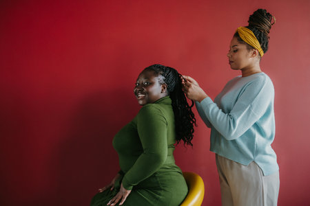 Confident African hairdresser braiding hair to a beautiful young smiling woman on red backgroundの写真素材