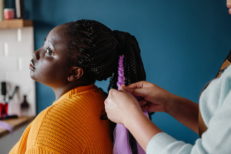 Close-up of hairdresser braiding hair to a young African woman in salonの写真素材