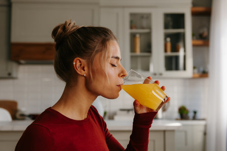 Side view of beautiful young woman enjoying fresh juice at the domestic kitchenの写真素材