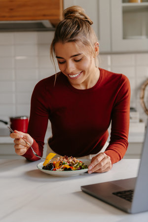 Smiling young woman enjoying healthy food for lunch at the domestic kitchenの写真素材