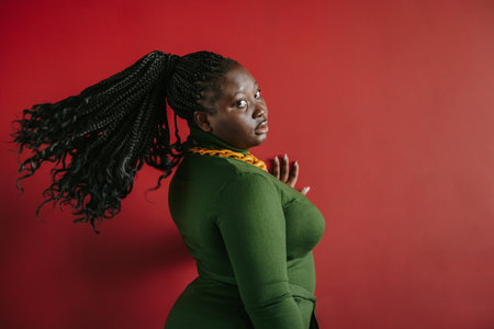 Beautiful plus size African woman with braided hair looking at camera on red backgroundの写真素材