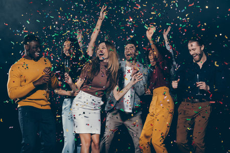 Group of young happy people enjoying champagne and throwing confetti while dancing in night clubの写真素材