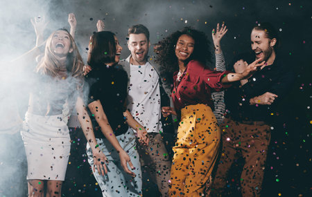 Group of joyful young friends dancing and throwing confetti while enjoying celebration in night clubの写真素材