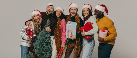 Joyful young people carrying Christmas tree and various ornaments on studio backgroundの写真素材