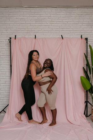 Two beautiful plus size African women in sportswear smiling while bonding on fabric backgroundの写真素材