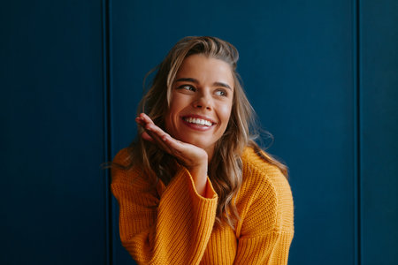 Cute young blond hair woman in yellow sweater looking away while standing on blue backgroundの写真素材