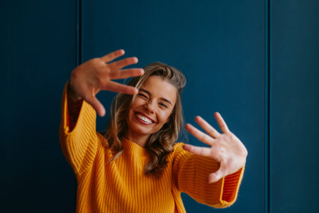 Blond hair woman in yellow sweater stretching out hand and smiling while standing on blue background