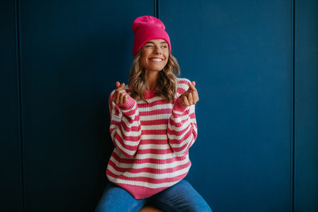 Playful young blond hair woman in casual wear snapping fingers and smiling on blue backgroundの写真素材