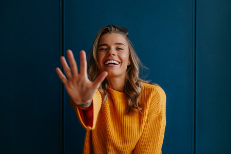 Cute young blond hair woman in yellow sweater smiling while standing on blue backgroundの写真素材