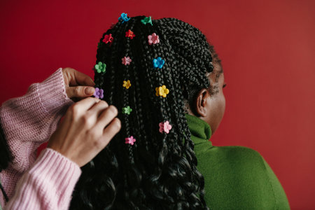 Close-up rear view of hairdresser putting on colorful clips on braided hair of African womanの写真素材