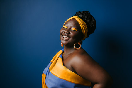 Beautiful plus size African woman wearing traditional African attire and smiling on blue backgroundの写真素材
