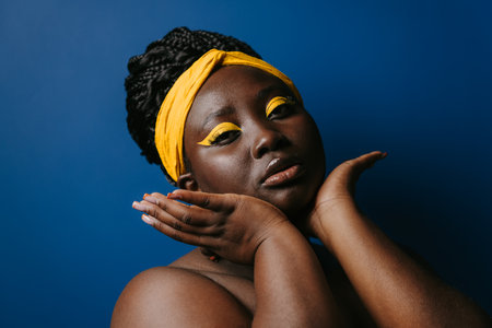 Portrait of confident African woman with beautiful make-up and touching face on blue backgroundの写真素材