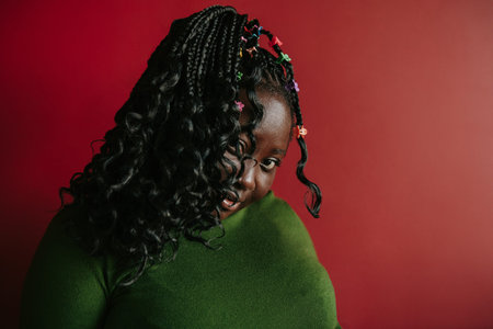 Confident African woman with braided hair and colorful clips looking at camera on red background