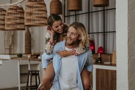 Playful young man piggybacking his happy girlfriend while having fun on at kitchen togetherの写真素材