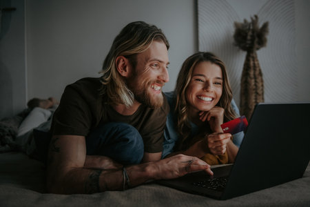 Happy loving couple looking at laptop and using credit card while shopping online from homeの写真素材