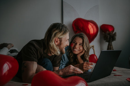 Joyful loving couple using laptop and shopping online at Valentines day from decorated bedroomの写真素材